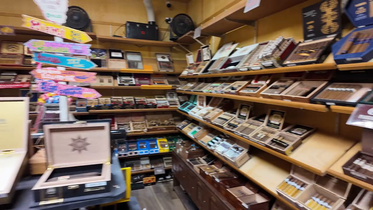 Shelves of cigar boxes inside the walk-in humidor, with a colorful beach-style signpost at the left.